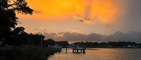 A sunset over a calm river with a dock and boats.