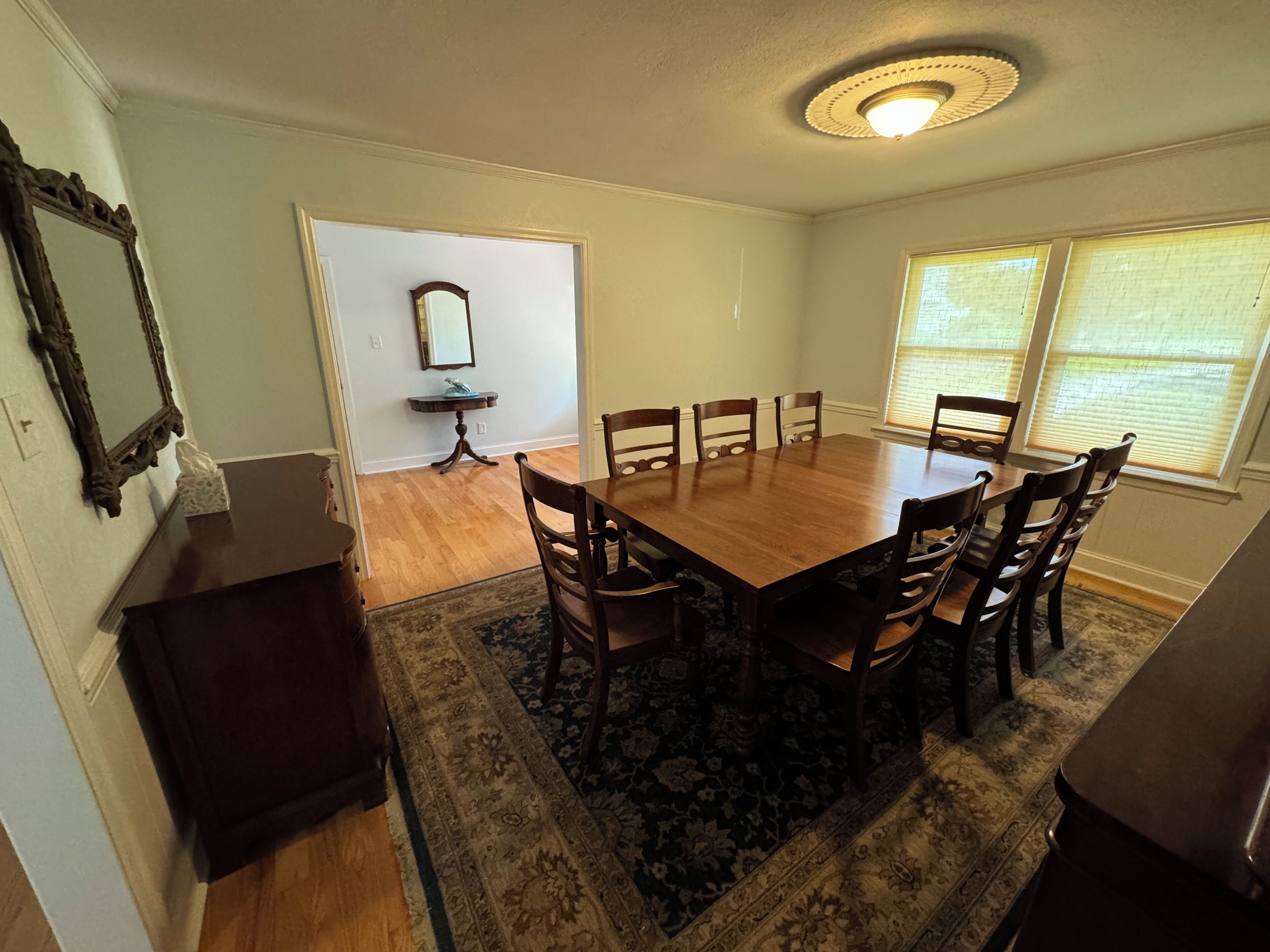 A dining room with a wooden table and chairs, a rug, a small side table, and a mirror on the wall.