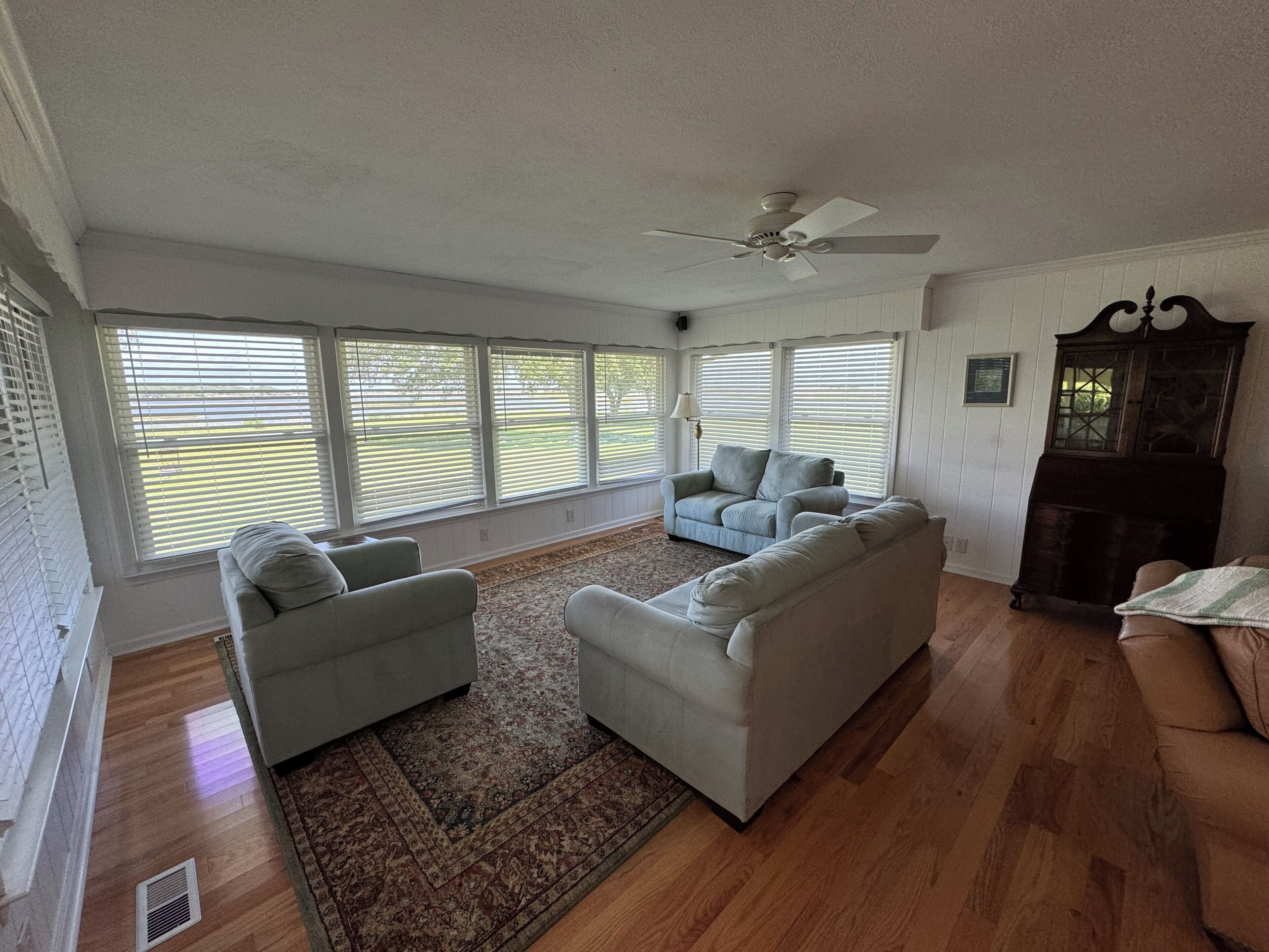 A living room with a large window, a ceiling fan, and a dark wooden cabinet.