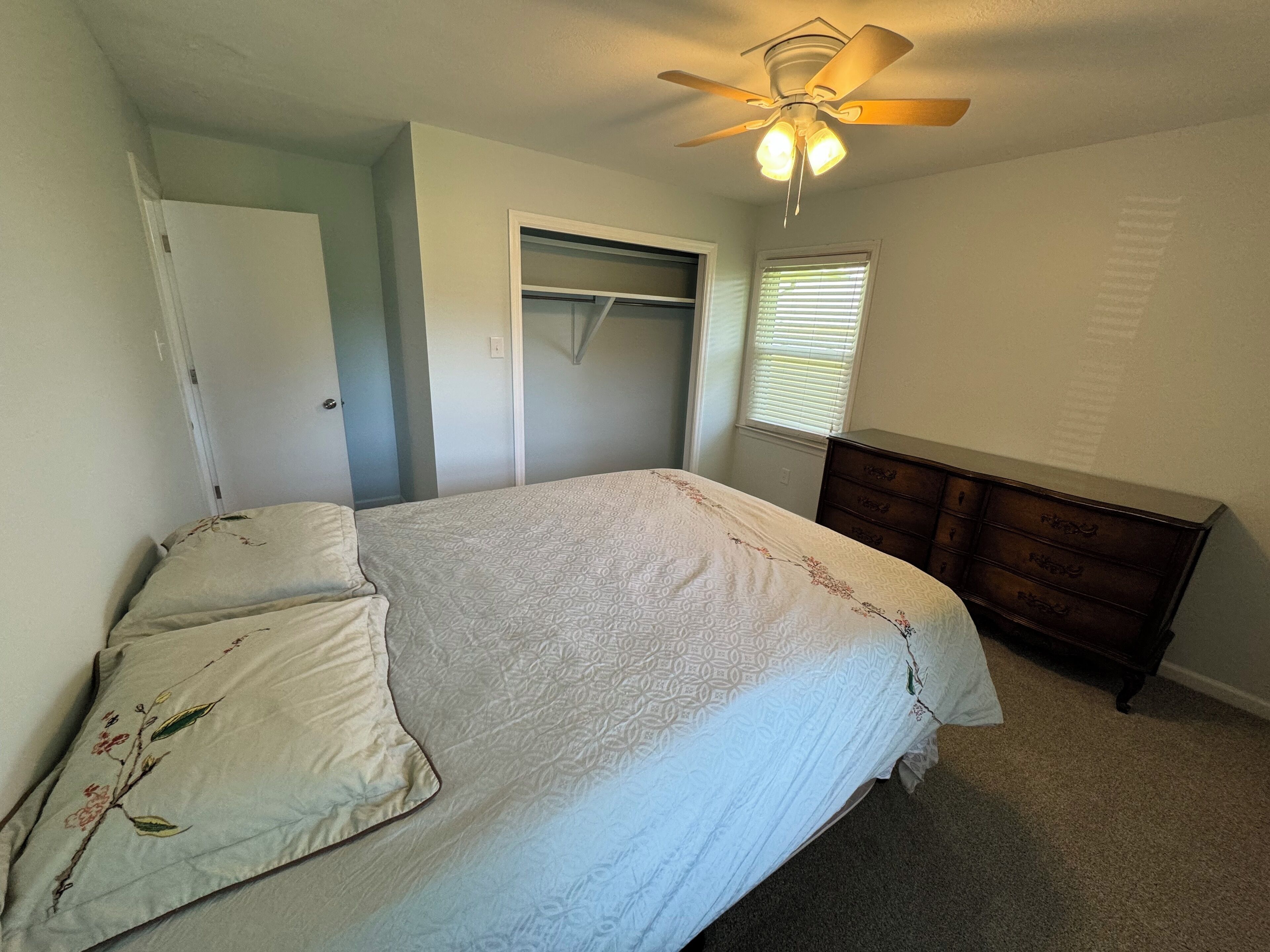 Een slaapkamer met een bed, een dressoir, een plafondventilator en een kast.