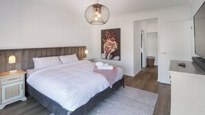 Una camera da letto moderna con un grande letto, comodini, una lampada a sospensione, un quadro e un televisore.