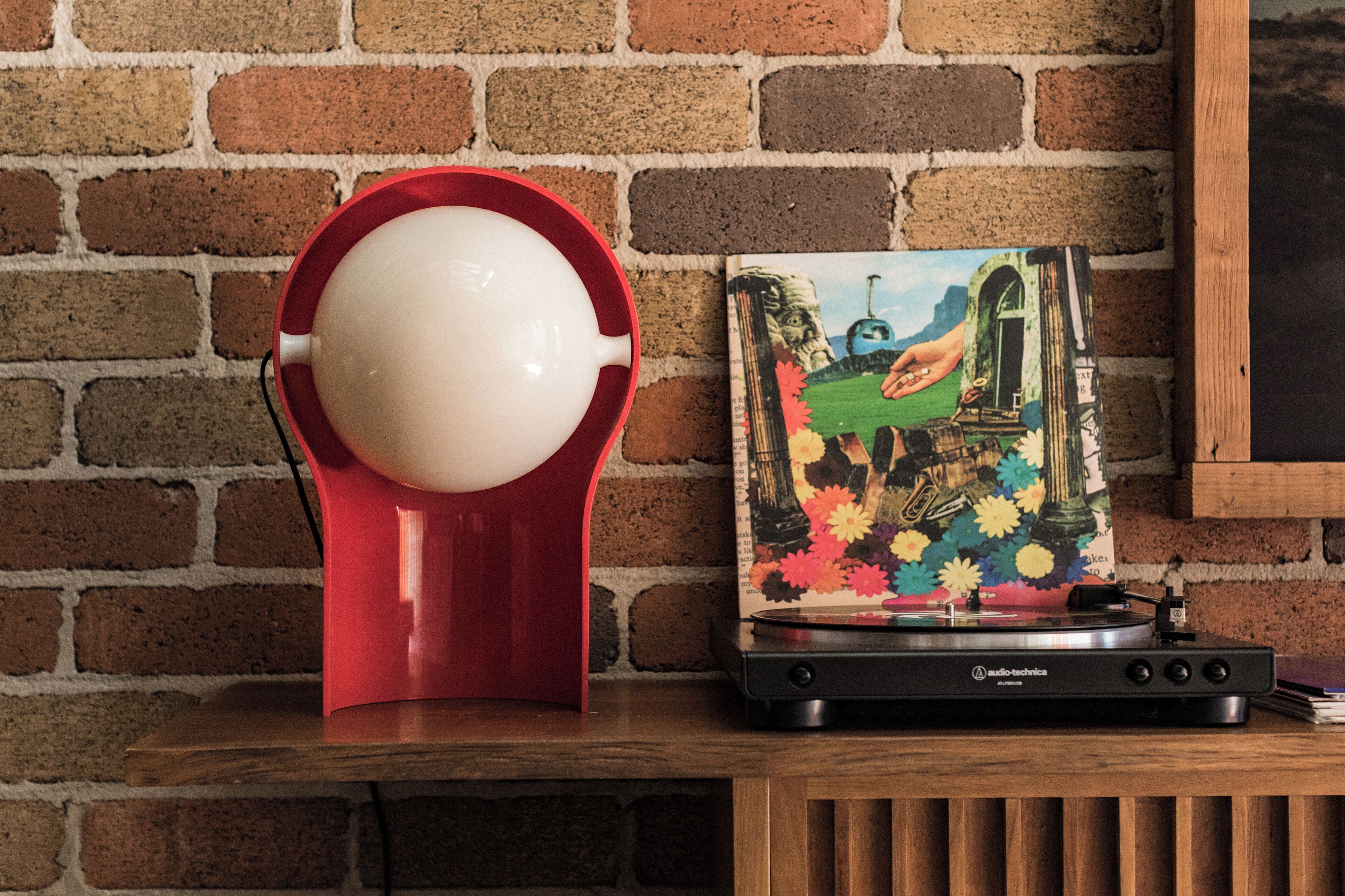 A red speaker on a wooden table against a brick wall.