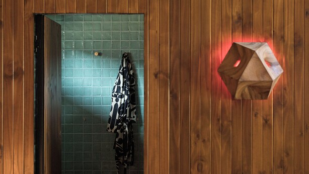 A wooden-paneled bathroom with a green-tiled wall, a towel rack with patterned towels, and a wooden object with a red light. - Sea Sea Hotel (Crescent Head)