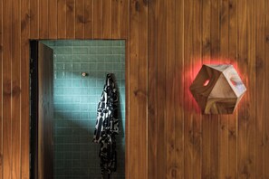 Ein Badezimmer mit Holzwandverkleidung, einer Wand in Grünem Fliesenmuster, einem Handtuchhalter mit gemusterten Handtüchern und einem Holzgegenstand mit roter Beleuchtung.