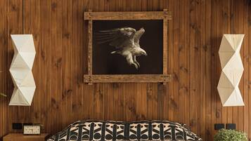 A room with wooden panel walls, a framed picture of an eagle, a bed with patterned bedding, a clock, and a small plant.