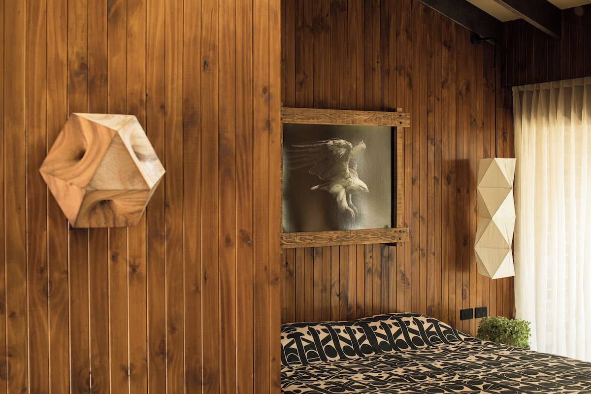 A wooden-paneled room with a bed, a framed picture, and a geometric wall decoration.