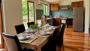 Un coin repas avec une table en bois, dressée pour quatre personnes et entourée de chaises, ainsi qu’une cuisine équipée de meubles et d’appareils électroménagers en bois.