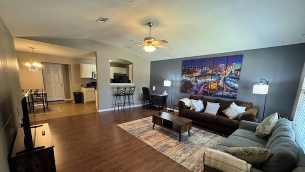 A spacious living room with a dark wood floor, a brown sofa, a coffee table, and a cityscape painting on the wall. - Amazing 3-bedroom home with 2 full baths. Spacious fenced backyard. WiFi present (Fort Smith)