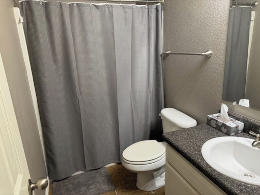 Bagno con tenda della doccia, water, lavandino e porta asciugamani.