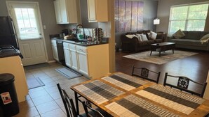 A dining area with a quilted table and chairs, a kitchen in the background, and a living room with a couch and coffee table. - Amazing 3-bedroom home with 2 full baths. Spacious fenced backyard. WiFi present (Fort Smith)