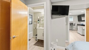 A modern apartment with a wooden door, a kitchen area with a TV, and a bathroom with a mirror and towel rack.