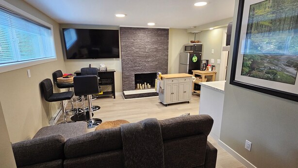 A modern living room with a TV, seating, a fireplace, and a kitchen area.