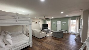 A room with bunk beds, a sofa, a television, and a ceiling fan.