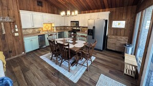 A rustic kitchen with wooden cabinets, a stainless steel refrigerator, and a dining area with a round table and chairs.
