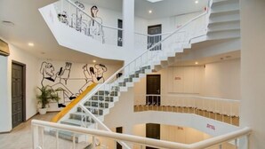 A multi-level interior with a central staircase, white railings, and a wall with line drawings. - Maitrayee Hotel - Nagpur (Nagpur)