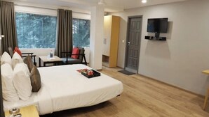 A hotel room with a bed, a TV mounted on the wall, a window with curtains, and a door. - Maitrayee Hotel - Nagpur (Nagpur)