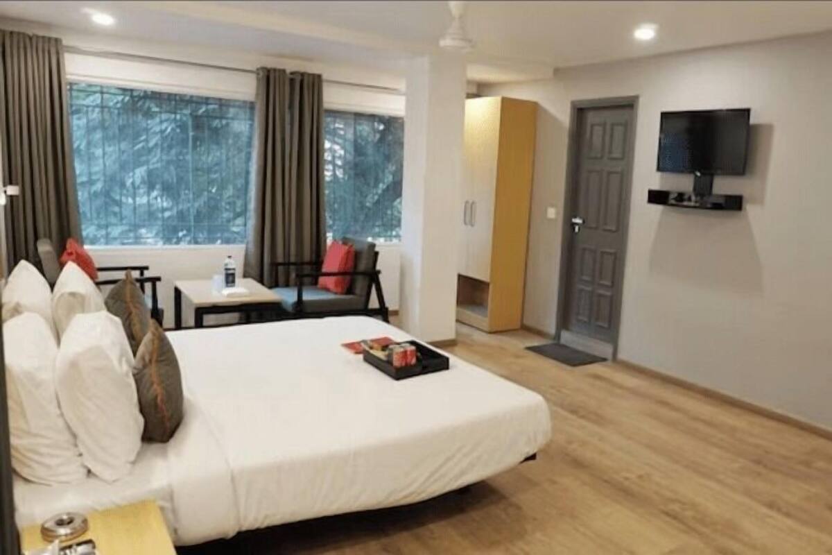 Ein Hotelzimmer mit Bett, Wandfernseher, Fenster mit Vorhängen und einer Tür.