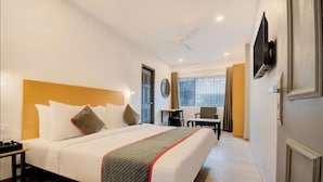A hotel room with a large bed, a desk, a chair, a TV, and a window with curtains. - Maitrayee Hotel - Nagpur (Nagpur)