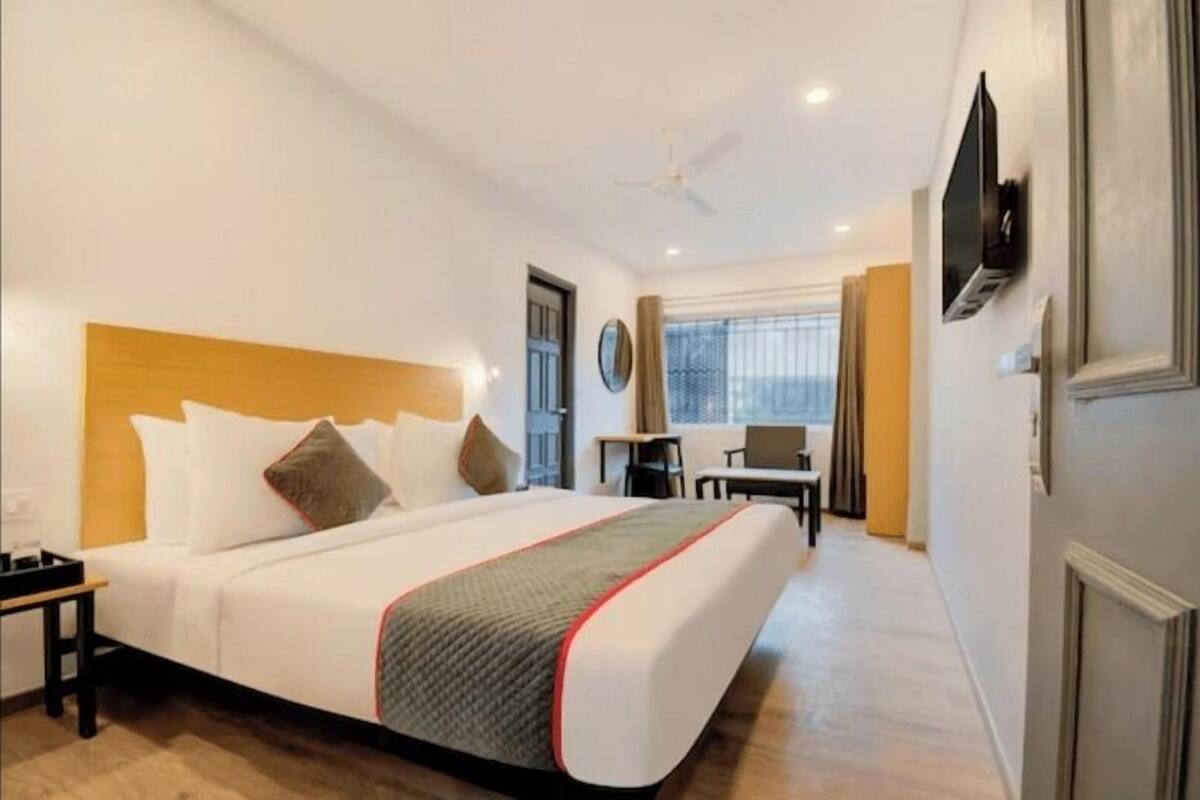 Ein Hotelzimmer mit einem großen Bett, einem Schreibtisch, einem Stuhl, einem Fernseher und einem Fenster mit Vorhängen.