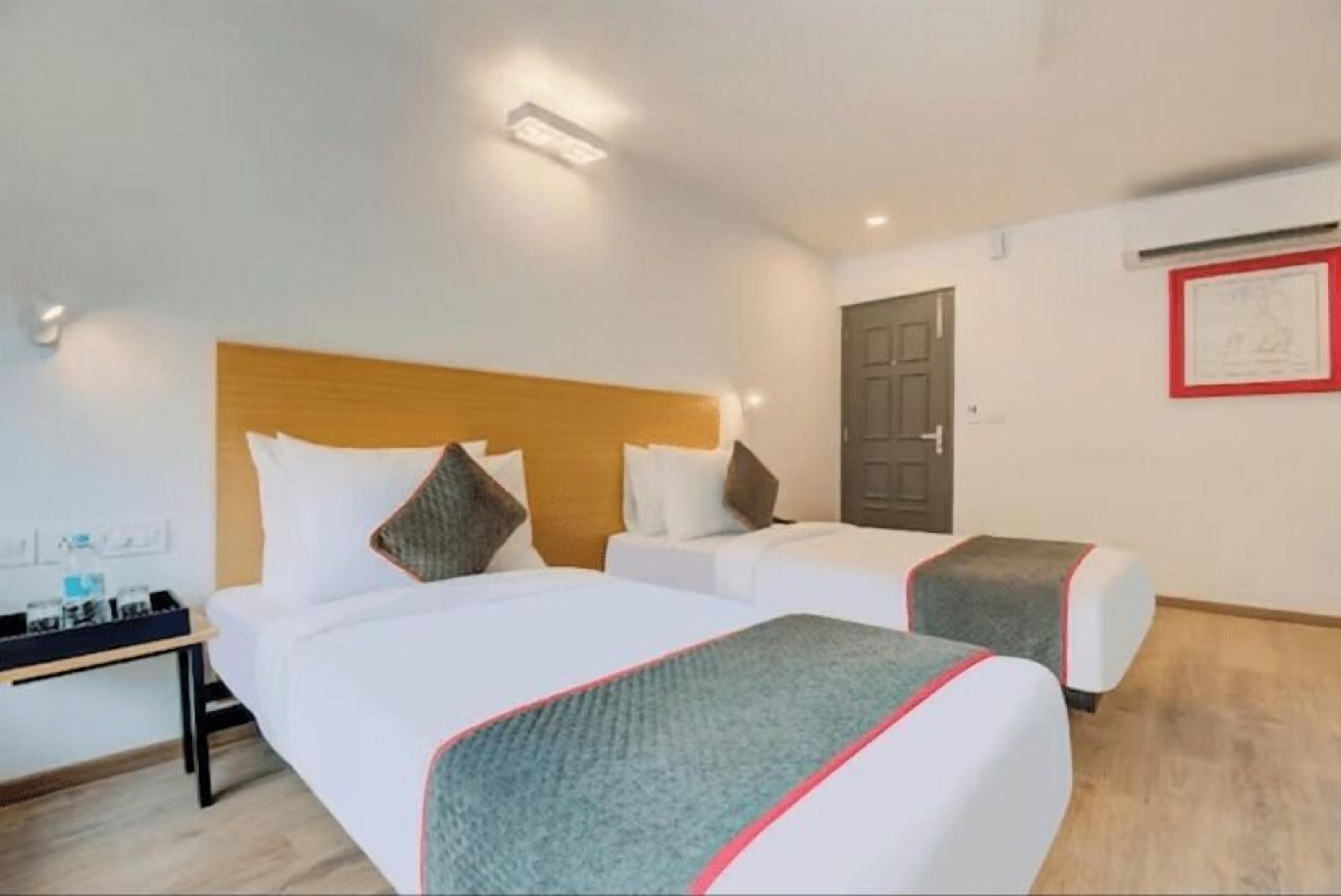 Habitación de hotel con dos camas, un cabecero de madera, una mesita de noche y una puerta.