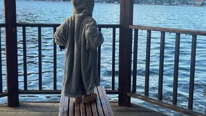 A wooden pier with a bench, overlooking a calm body of water and a mountainous landscape.