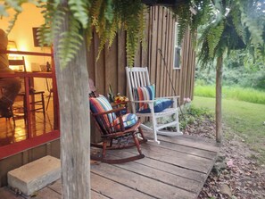 Eine Holzterrasse mit zwei Schaukelstühlen, einer mit bunten Kissen und einer mit gestreiftem Kissen.
