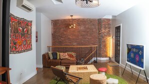 Un salón acogedor con pared de ladrillo, sofá de cuero marrón, alfombra verde y una pequeña mesa de madera.