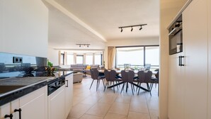 Uma cozinha moderna com área de refeições, janelas amplas e vista para o mar.