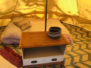 Cozy tent interior with a neatly made bed, wooden nightstand, and vibrant rug.