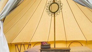 A tent with a bed, a small table, and a hanging mirror. - Bell Tent , Carreglwyd Estate, Anglesey (Llanfaethlu,)