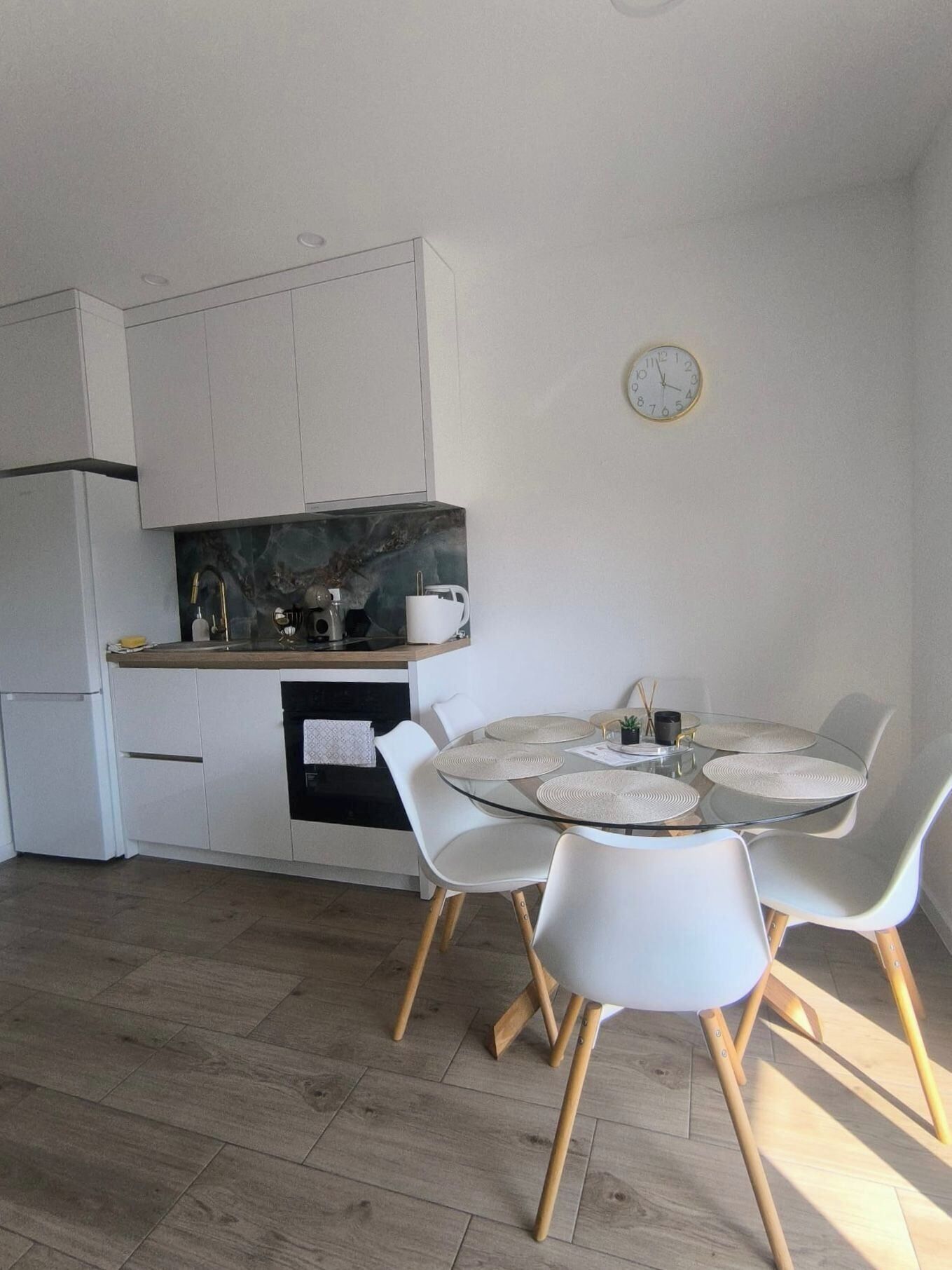 A modern kitchen with white cabinets, a marble countertop, and a round glass table with white chairs.