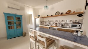 A modern kitchen with a blue cabinet, white chairs, a marble countertop, and a microwave. - Villa Aroi just a stone's throw from the sea! (Sicilia)