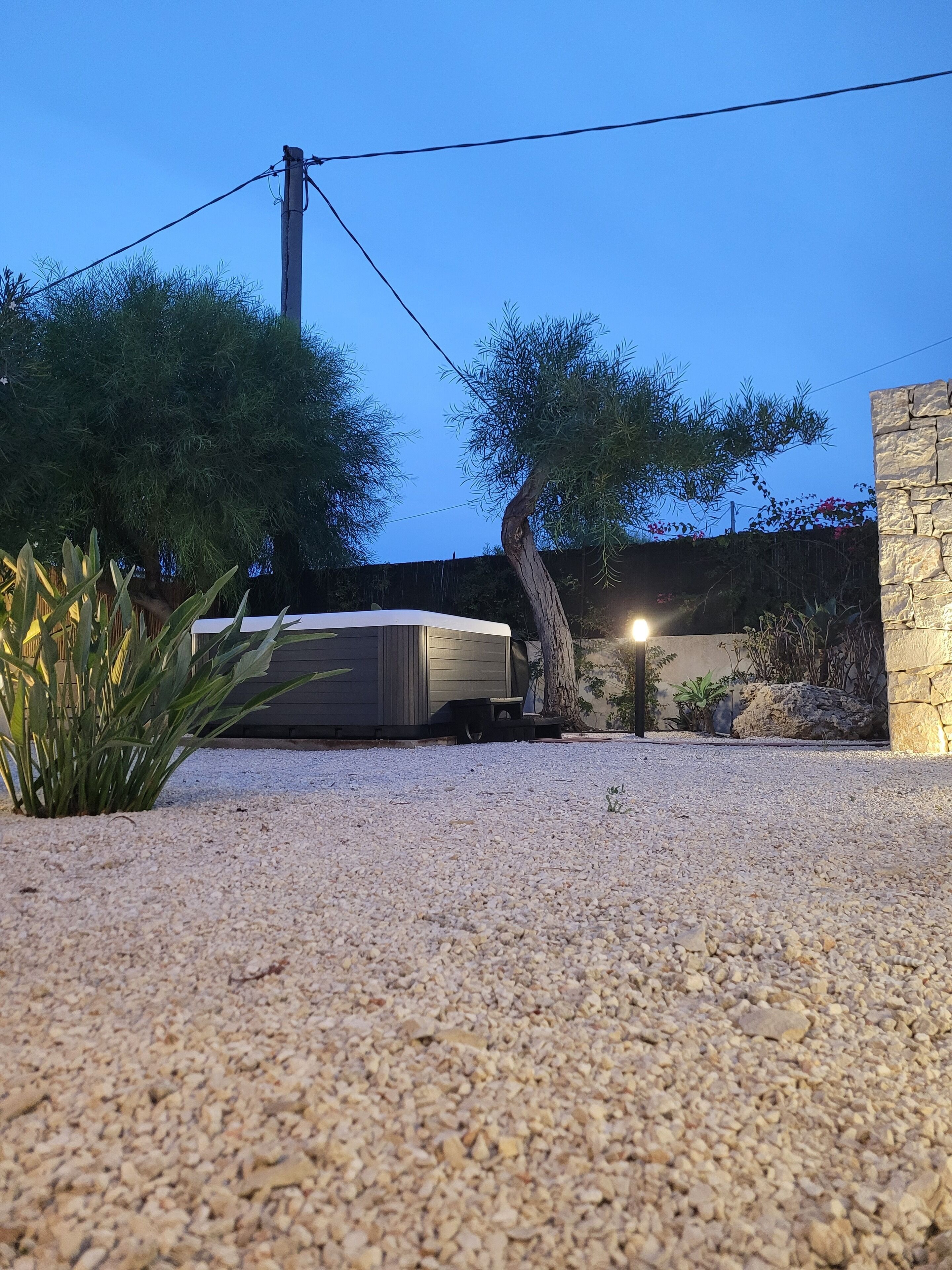 A gravel driveway leading to a covered outdoor area with a stone wall and a tree.
