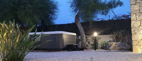 A gravel driveway leading to a covered outdoor area with a stone wall and a tree.