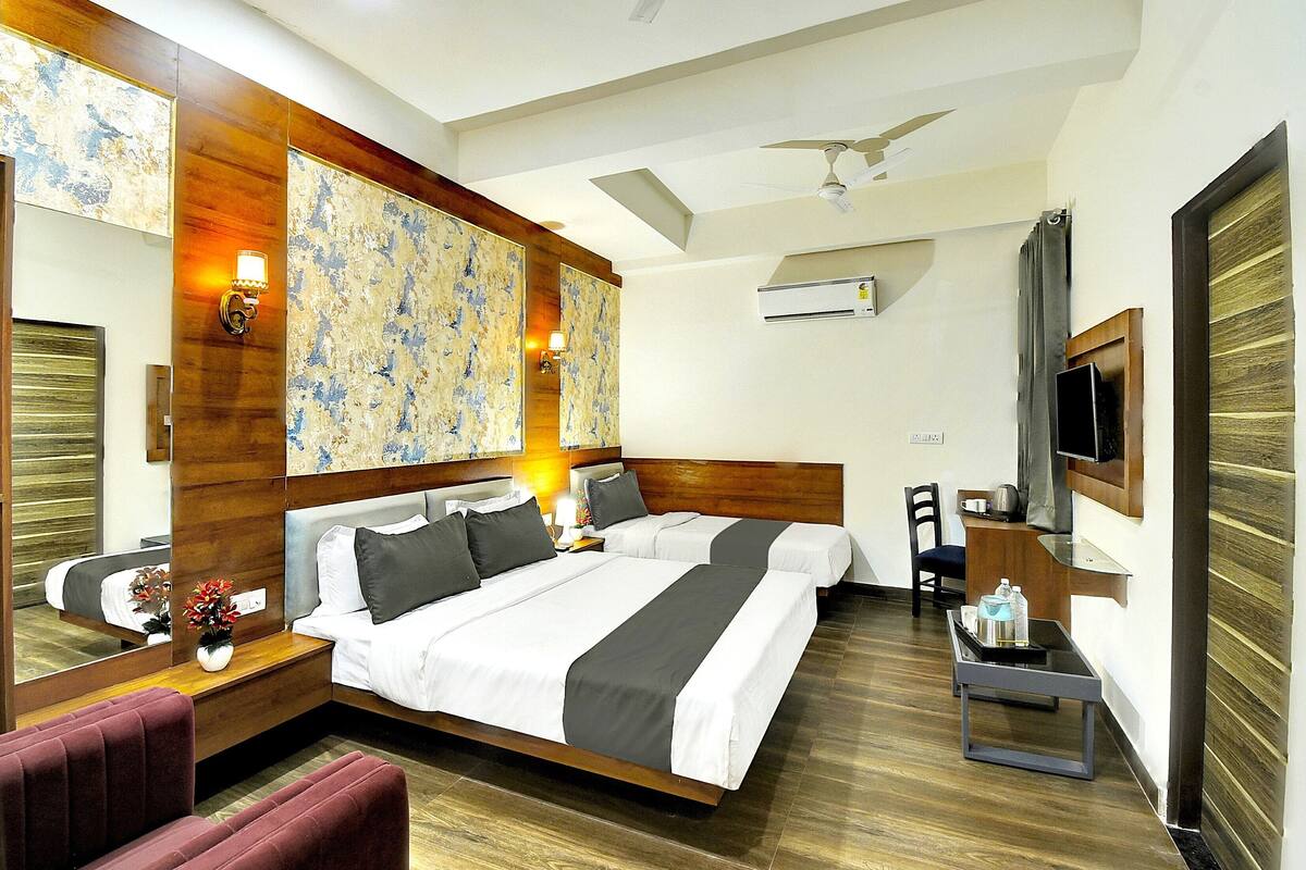 A hotel room with a large bed, a desk, a chair, a TV, and a ceiling fan.