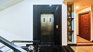 An elevator with a black marble wall and a metallic finish, a staircase with a metal handrail, and a wooden door with a patterned design. - Hotel Travaasa Inn (Jaipur)