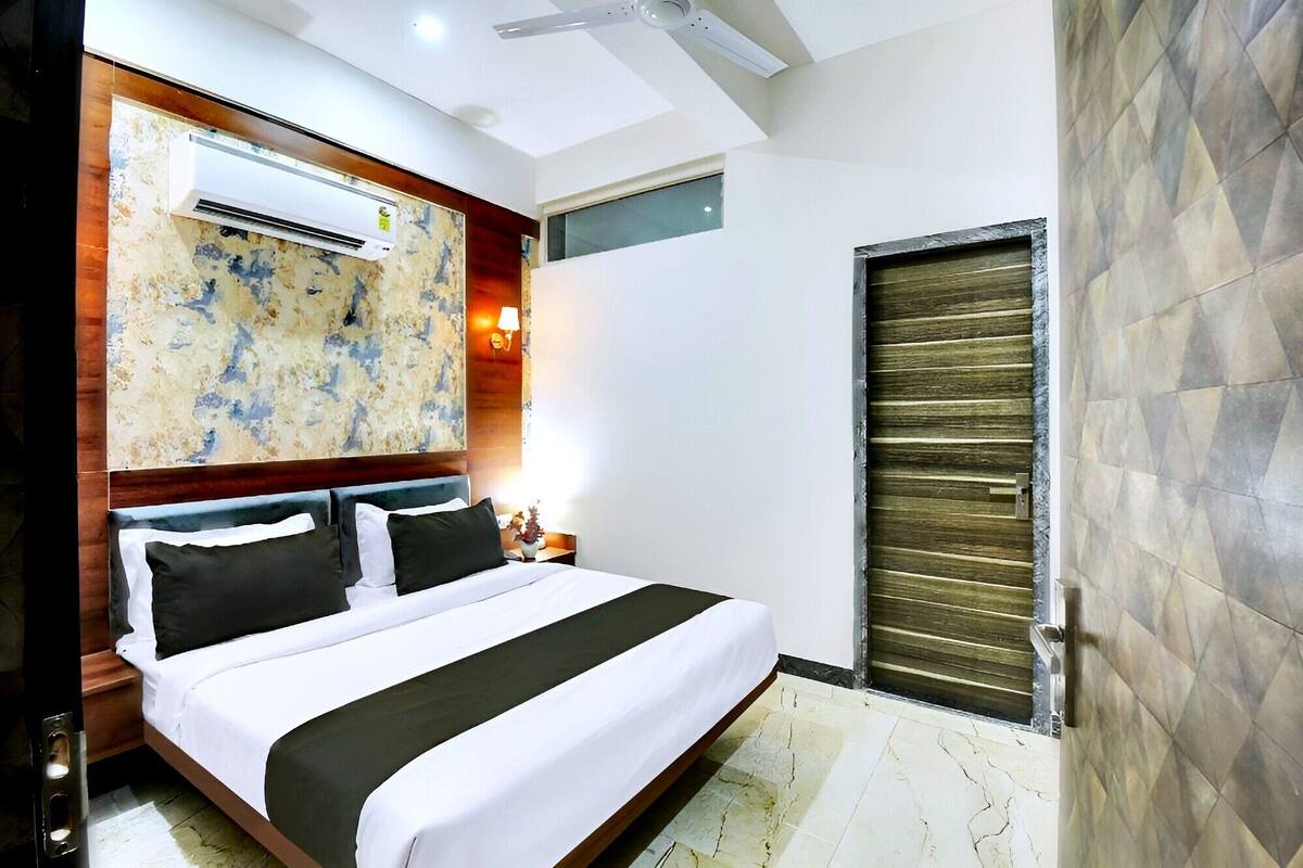 A modern hotel room with a large bed, an air conditioning unit, a ceiling fan, a decorative wall, and a sliding door.