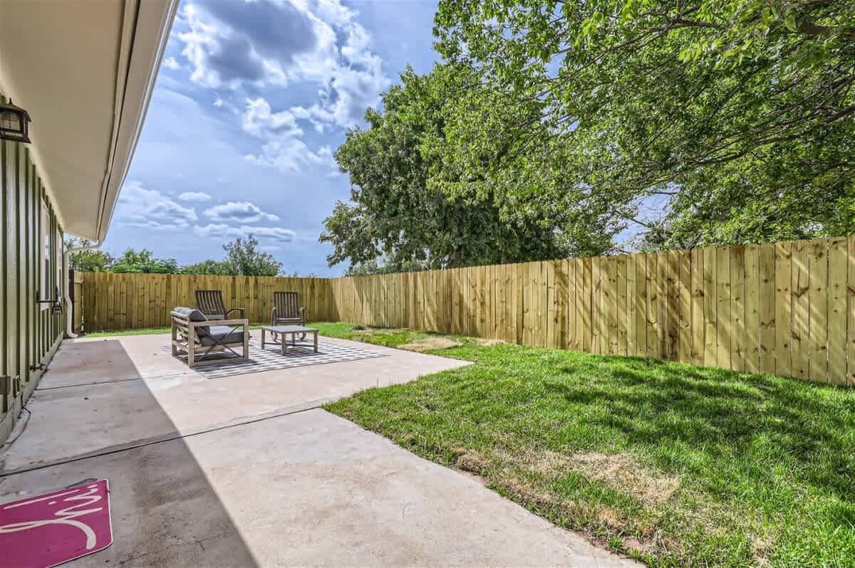 A backyard with a wooden fence, two lawn chairs, and a concrete patio.