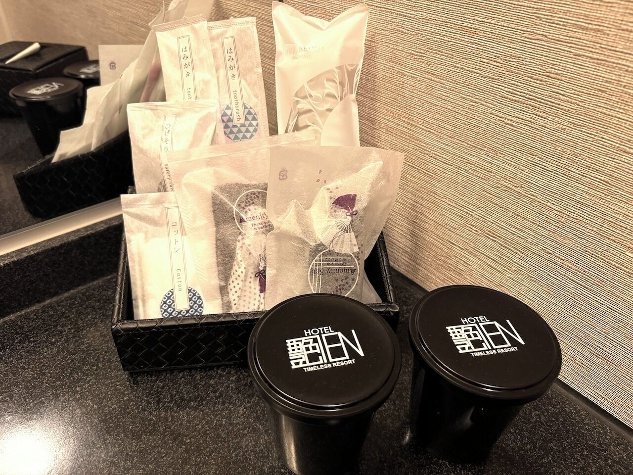 A tray of toiletries including a toothbrush, toothpaste, and cotton swabs. There are two black containers with the hotel name on them.