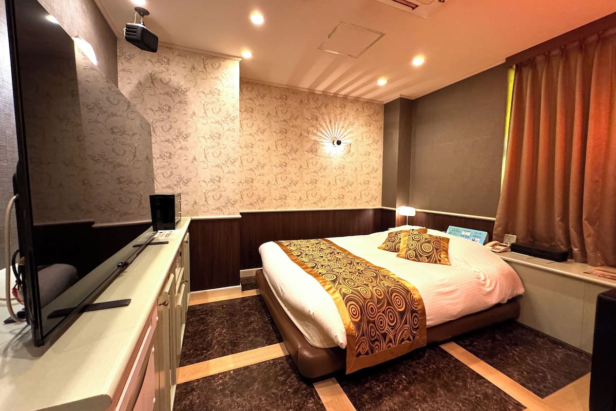 A hotel room with a bed, bedside table, and a desk with a computer.