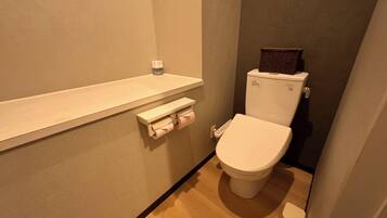 A small, compact bathroom with a toilet, a shelf with a bottle, and a toilet paper holder.