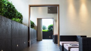 Um corredor moderno com piso ladrilhado, um rebordo baixo com vegetação e um espaço de estar com mobiliário de vime.