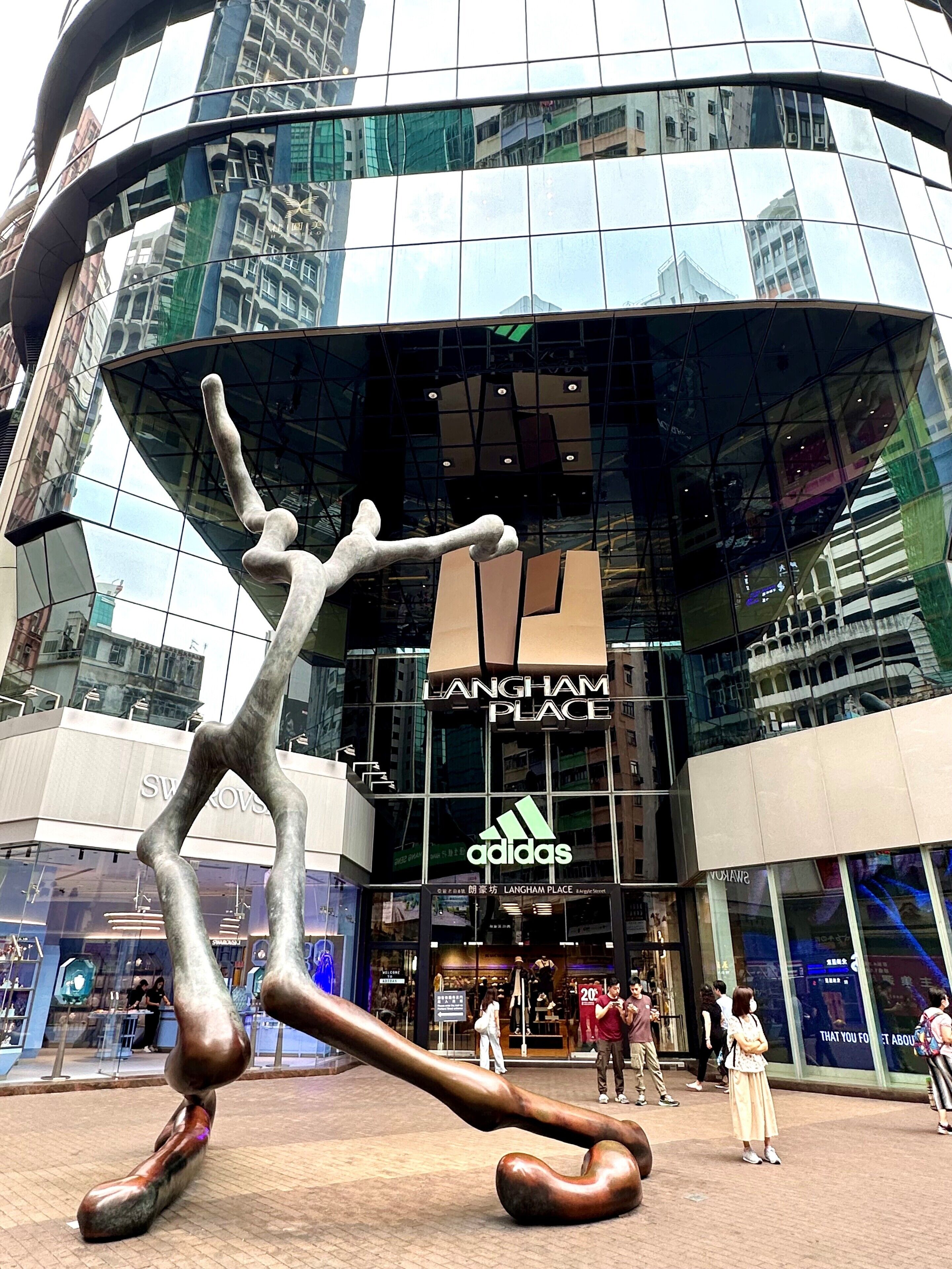 Un bâtiment moderne à la façade incurvée en verre, sur lequel on peut voir les enseignes « LANGHAM PLACE » et « adidas ».