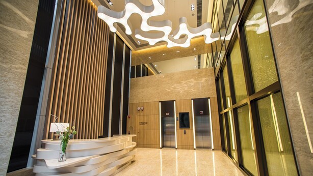 Um hall moderno com um balcão de atendimento curvo, uma escada e um conjunto de elevadores.