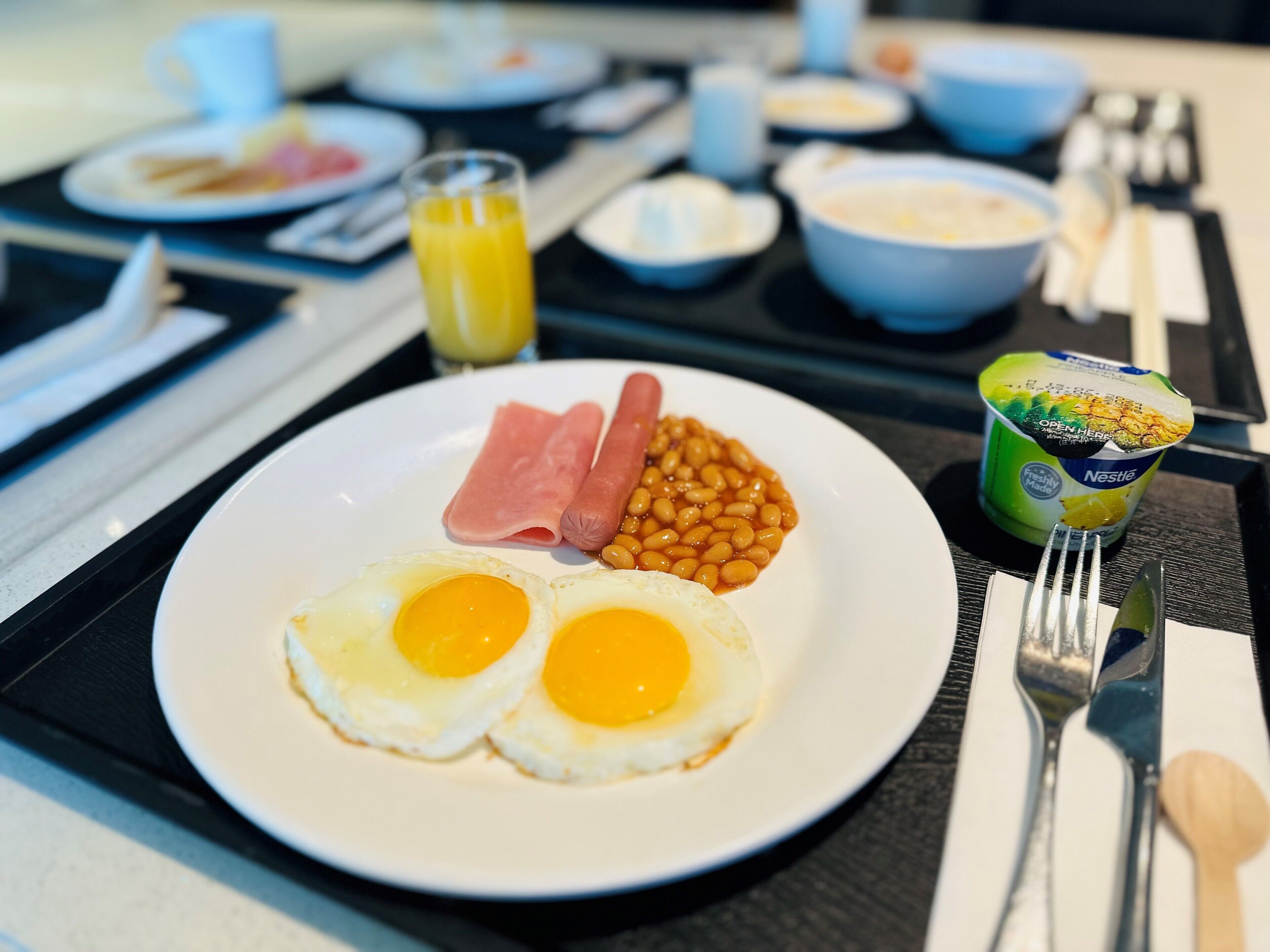Ein Frühstücksbrett mit Eiern, Bohnen, Schinken und einem Becher Joghurt.