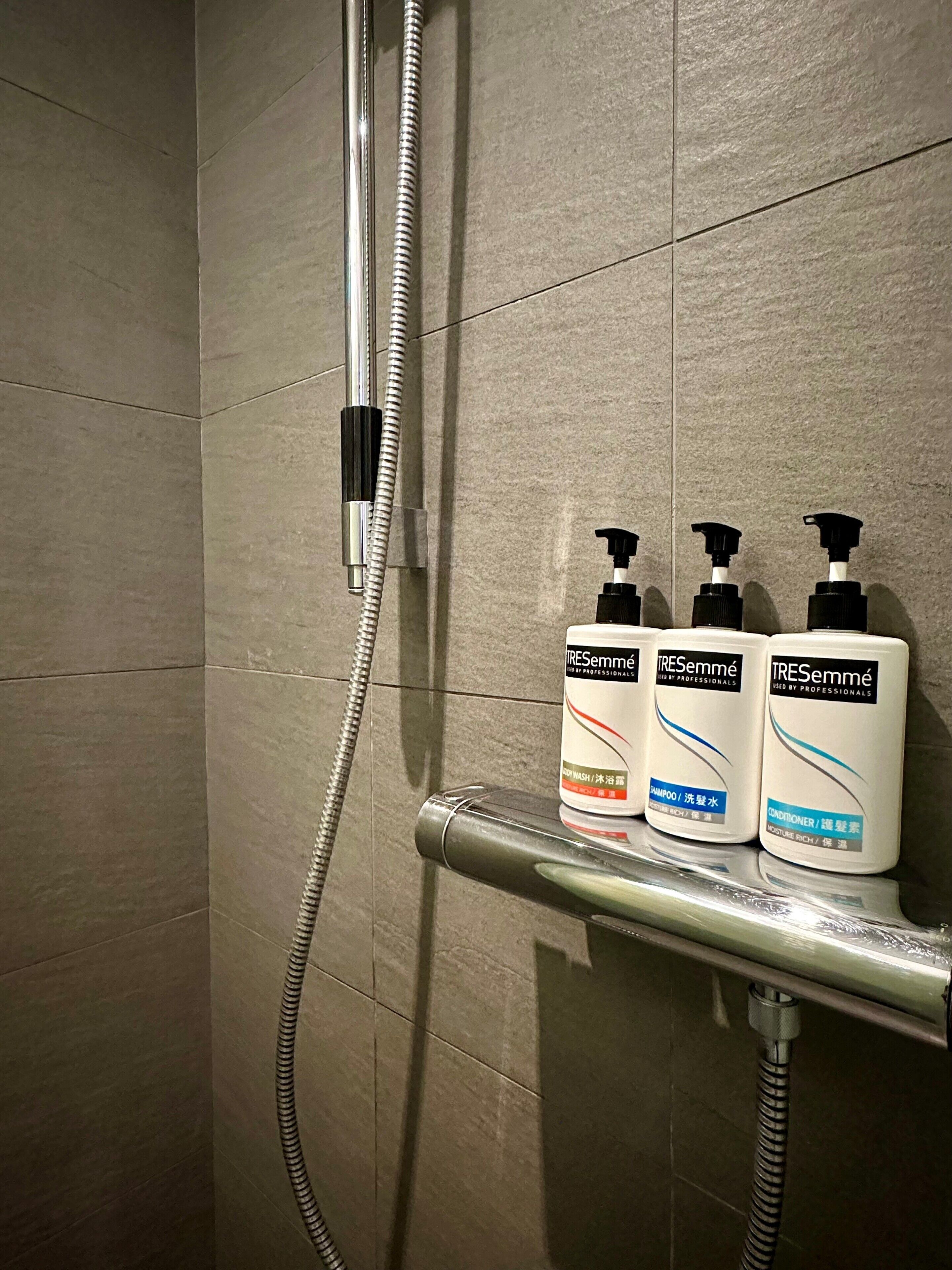 A shower area with a handheld showerhead and three bottles of TRESemmé body wash on a shelf.