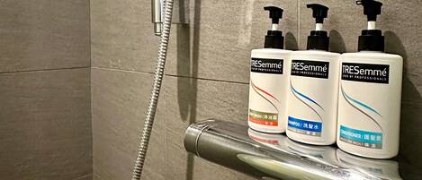 A shower area with a handheld showerhead and three bottles of TRESemmé body wash on a shelf.