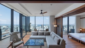 Une chambre d’hôtel moderne dotée d’un grand canapé d’angle, d’une table basse en marbre et offrant une vue sur la ville grâce à de grandes fenêtres du sol au plafond.