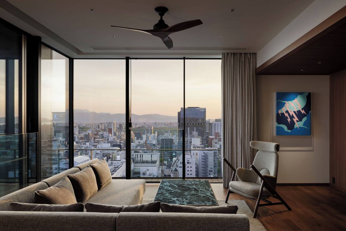 Un salon moderne doté d’une grande fenêtre donnant sur la ville, d’un ventilateur de plafond et d’un fauteuil contemporain.