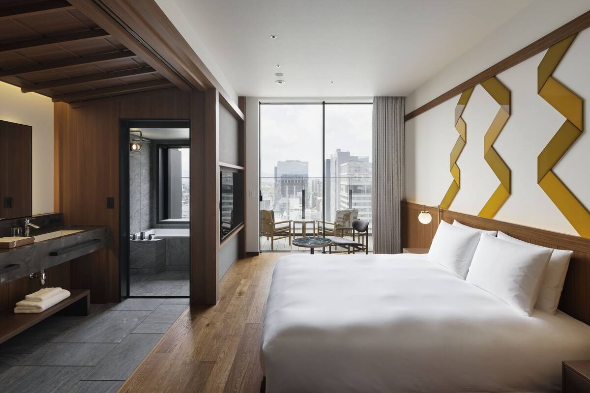 Une chambre d’hôtel avec un grand lit, une salle de bain avec baignoire, une coiffeuse en bois et une vue sur la ville.